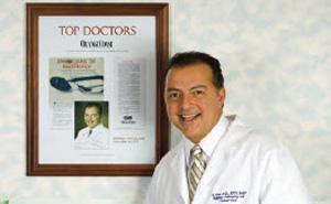 Dr Reda Smiling in front of framed top doctors article