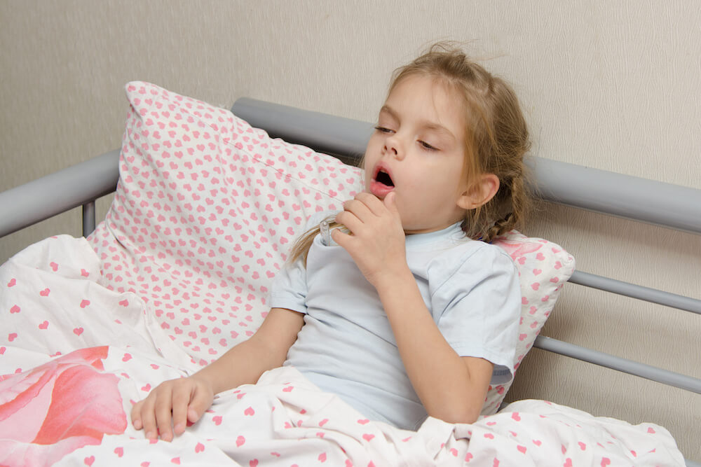 child coughing in bed on a pink pillow