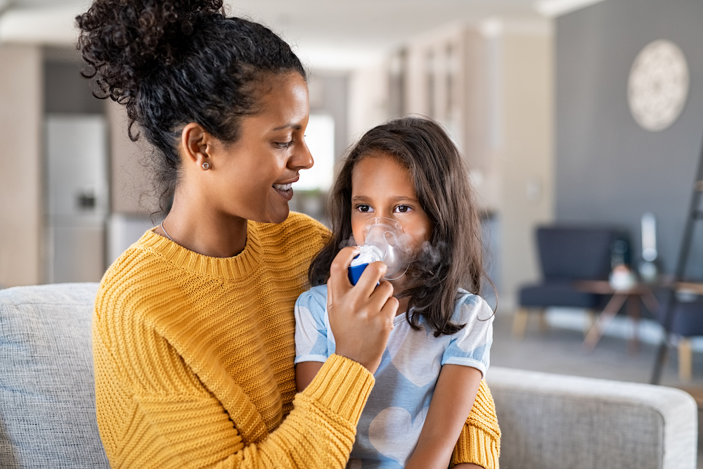 girl with chronic asthma getting an inhaler treatment from her mom