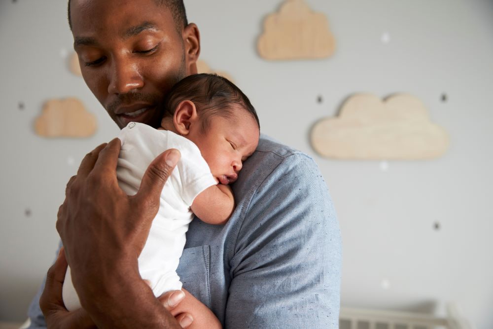 A father rocking his newborn child to help soothe the baby's discomfort.