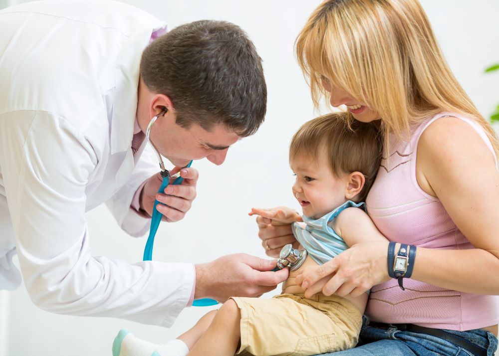 A doctor checking a child's heartbeat and breathing while the mother holds the child.