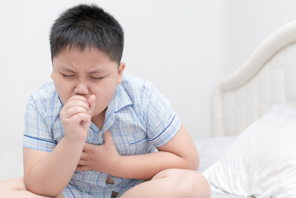 Sick obese boy is coughing and throat infection on bed, health care concept