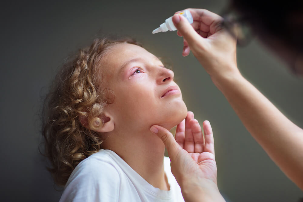 child with pink eye getting medicated eyedrops